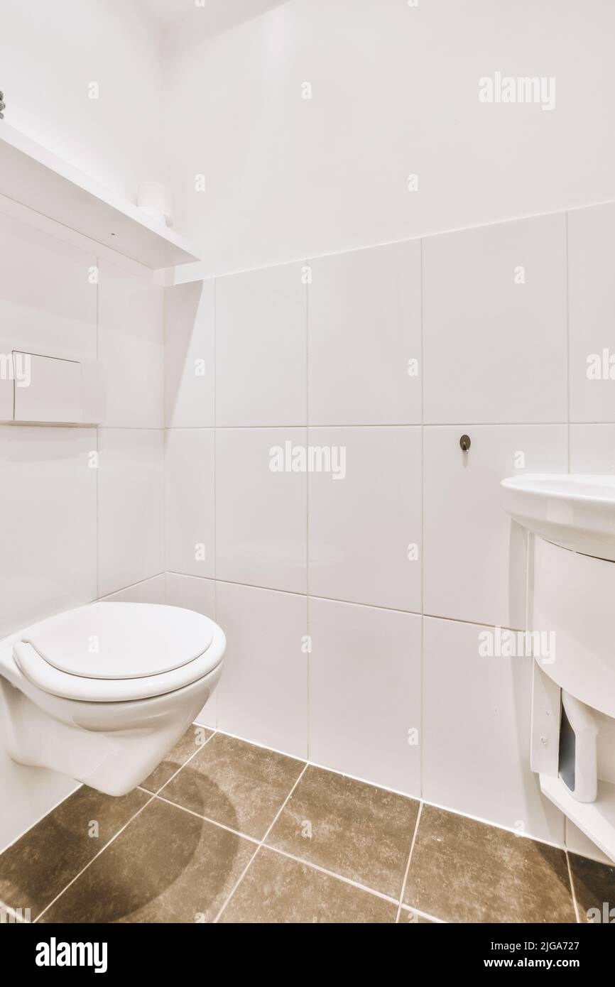 Wall hung toilet and small sink in corner in lavatory room with beige