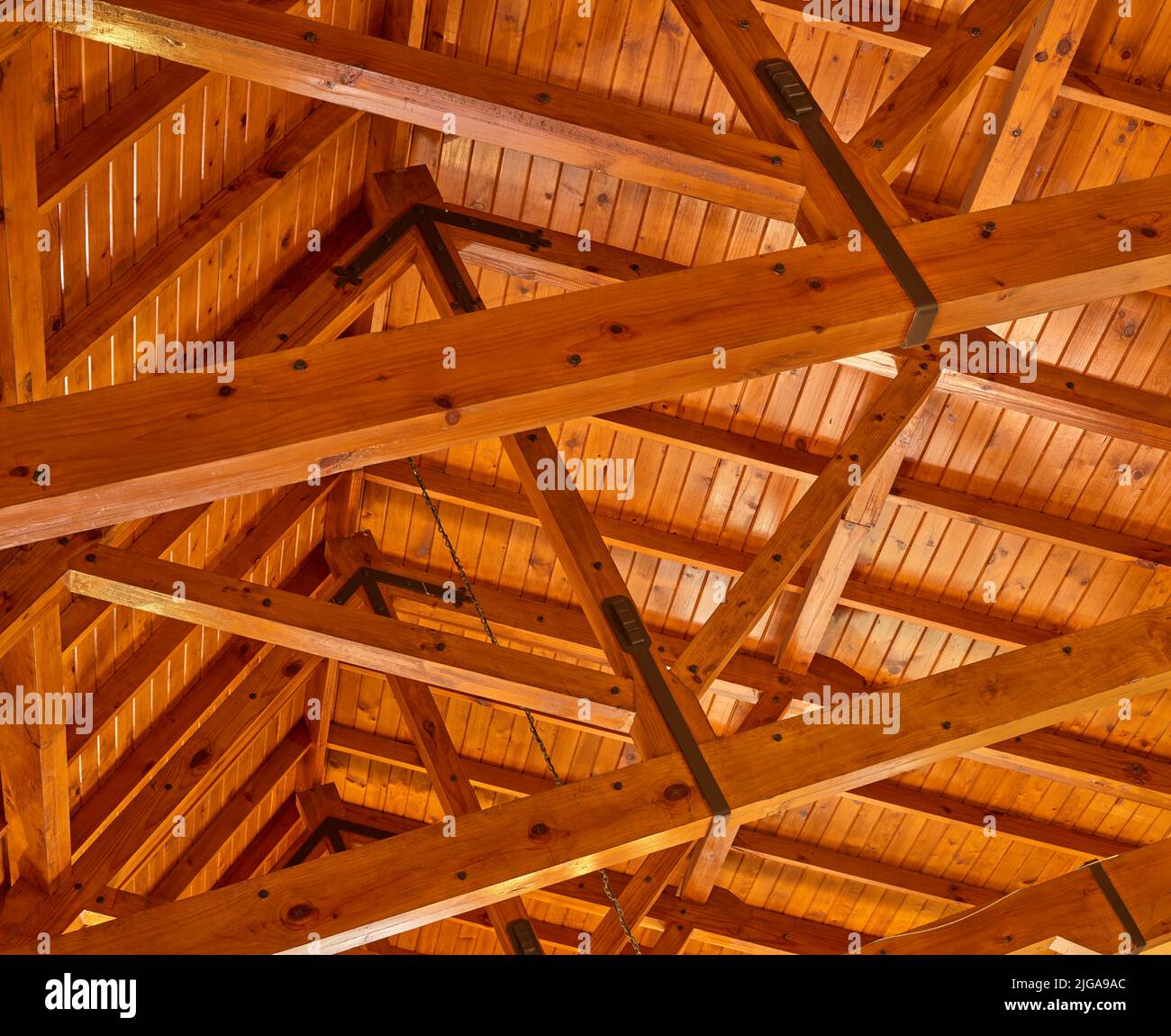 Crossed wood support trestles with their angle supporters on a ceiling. Closeup of roof rafters and cross beams of a shelter. Crossed thick beige Stock Photo