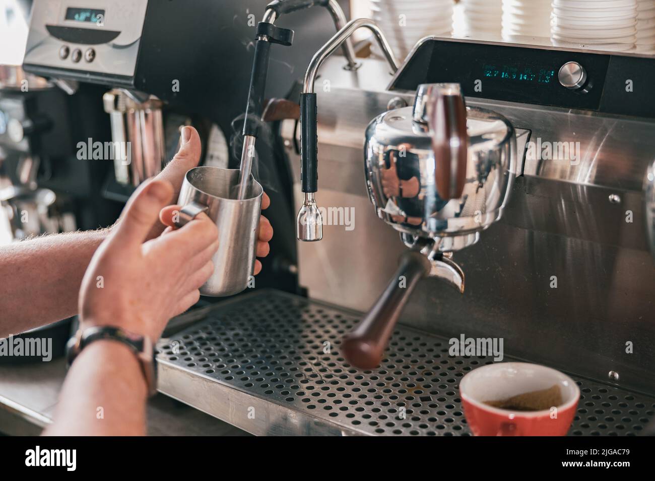Professional barista warming milk In metal jug with steam of coffee