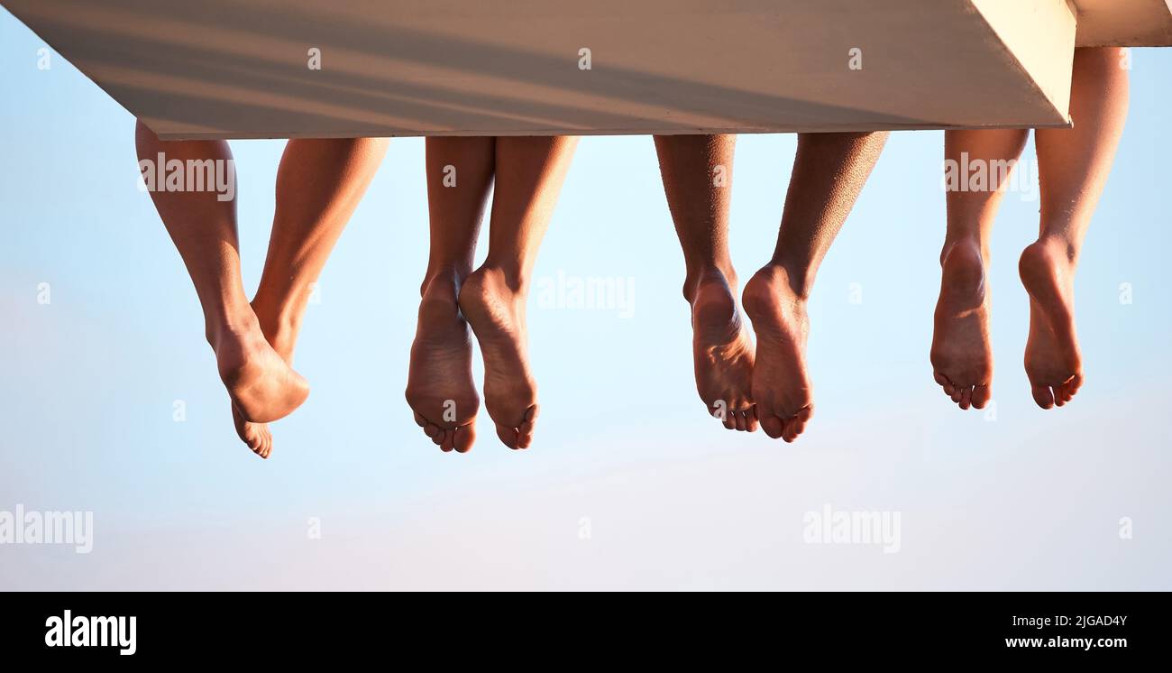 Poolside friends. Rearview shot of three unrecognizable swimmers sitting on a diving board. Stock Photo