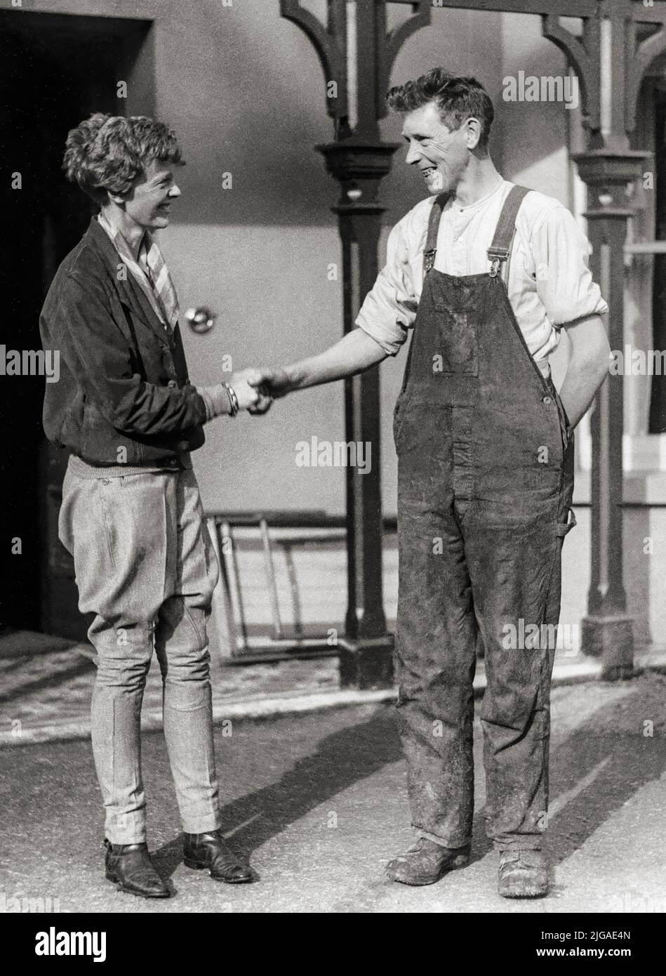 Amelia Earhart (1897 - declared dead 1939). She flew solo across the Atlantic in 1928, the first woman to do so. This photograph shows her shaking hands with Dan McCallon, the Irish farmer who was the only eyewitness to her landing in her Lockheed Vega. Upon greeting her, McCallon asked, 'Have you flown far?' Earhart answered, 'From America.' Stock Photo