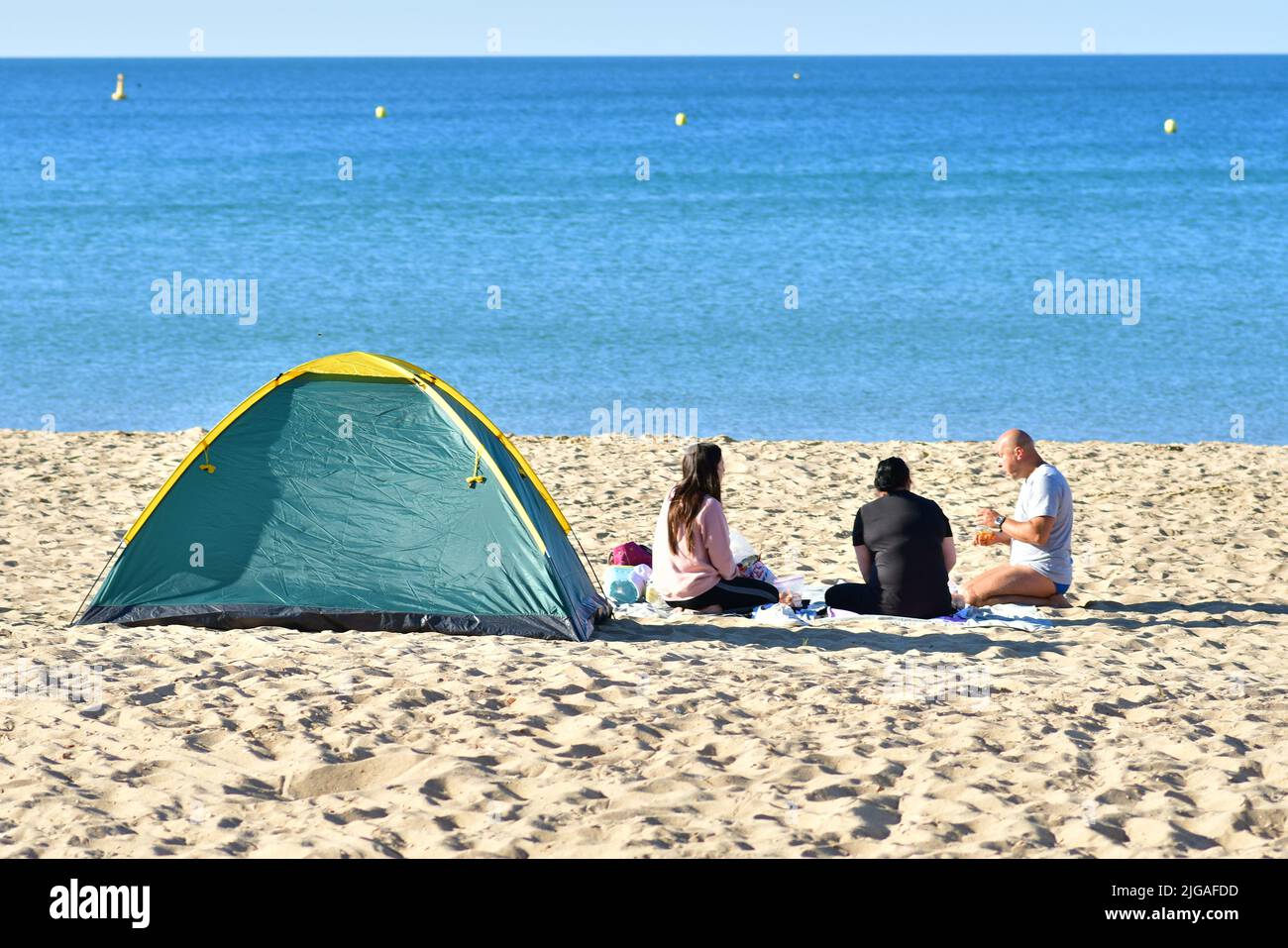 Boscombe, Bournemouth, Dorset, England, UK, 9th July 2022, Weather. Heatwave in mid-summer. People arrive at the beach before 8 am on Saturday morning. Temperatures will reach the high 20s by afternoon in wall-to-wall sunshine. People sitting on the beach with a tent. Credit: Paul Biggins/Alamy Live News Stock Photo