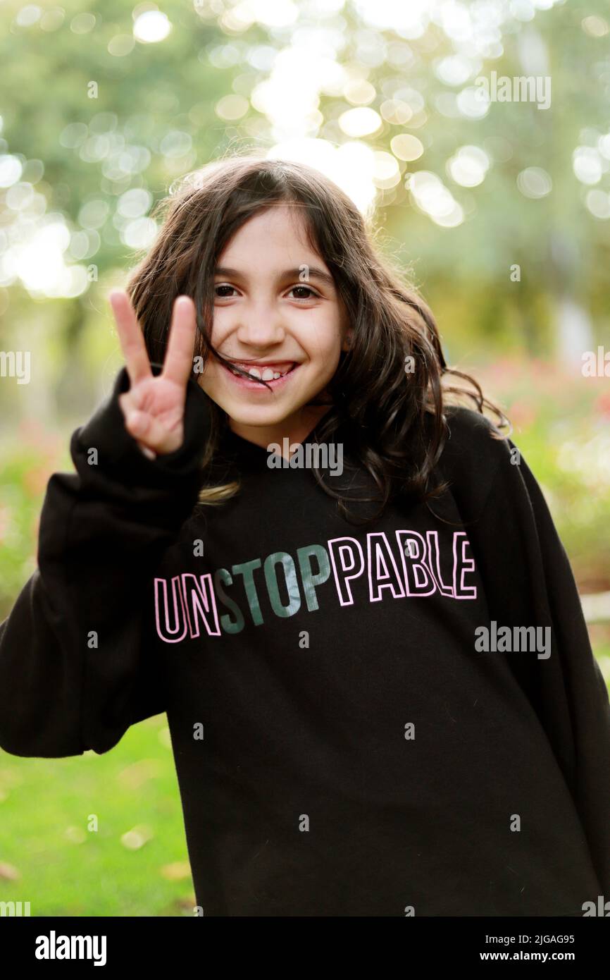 8 year old brunette girl with smile looking at camera and making the peace sign on location Stock Photo