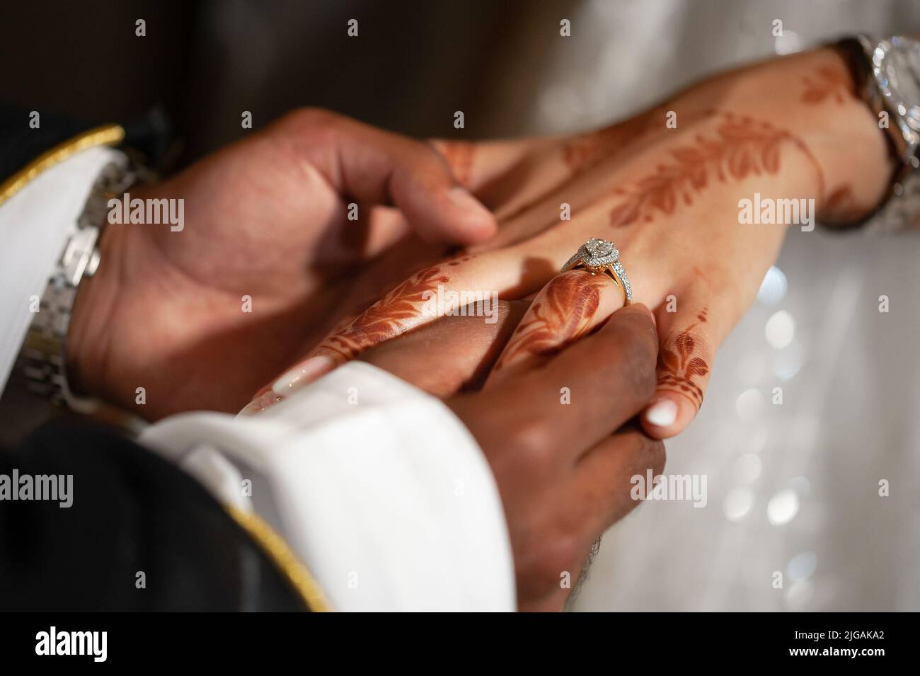 Man's hand slides diamond teardrop ring onto woman's finger. Arabic wedding with groom wearing bisht over kandora and bride's hands with henna tattoo. Stock Photo