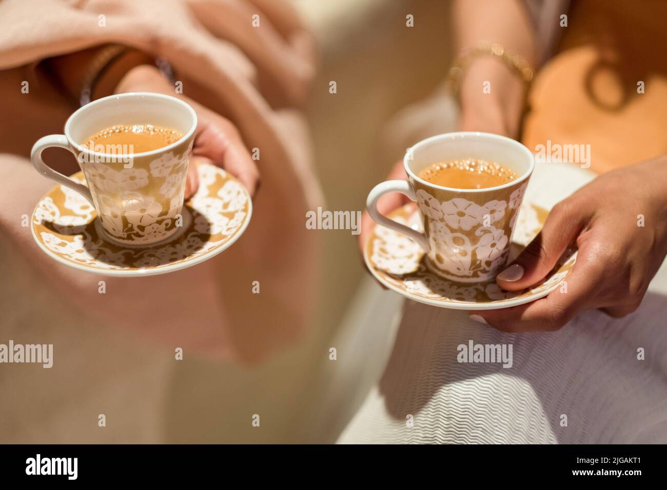 Female guests hold tiny cups of Masala Chai (or Karak Tea) at an Arabic wedding. This traditional Qatari drink, spiced tea with milk, came from India. Stock Photo
