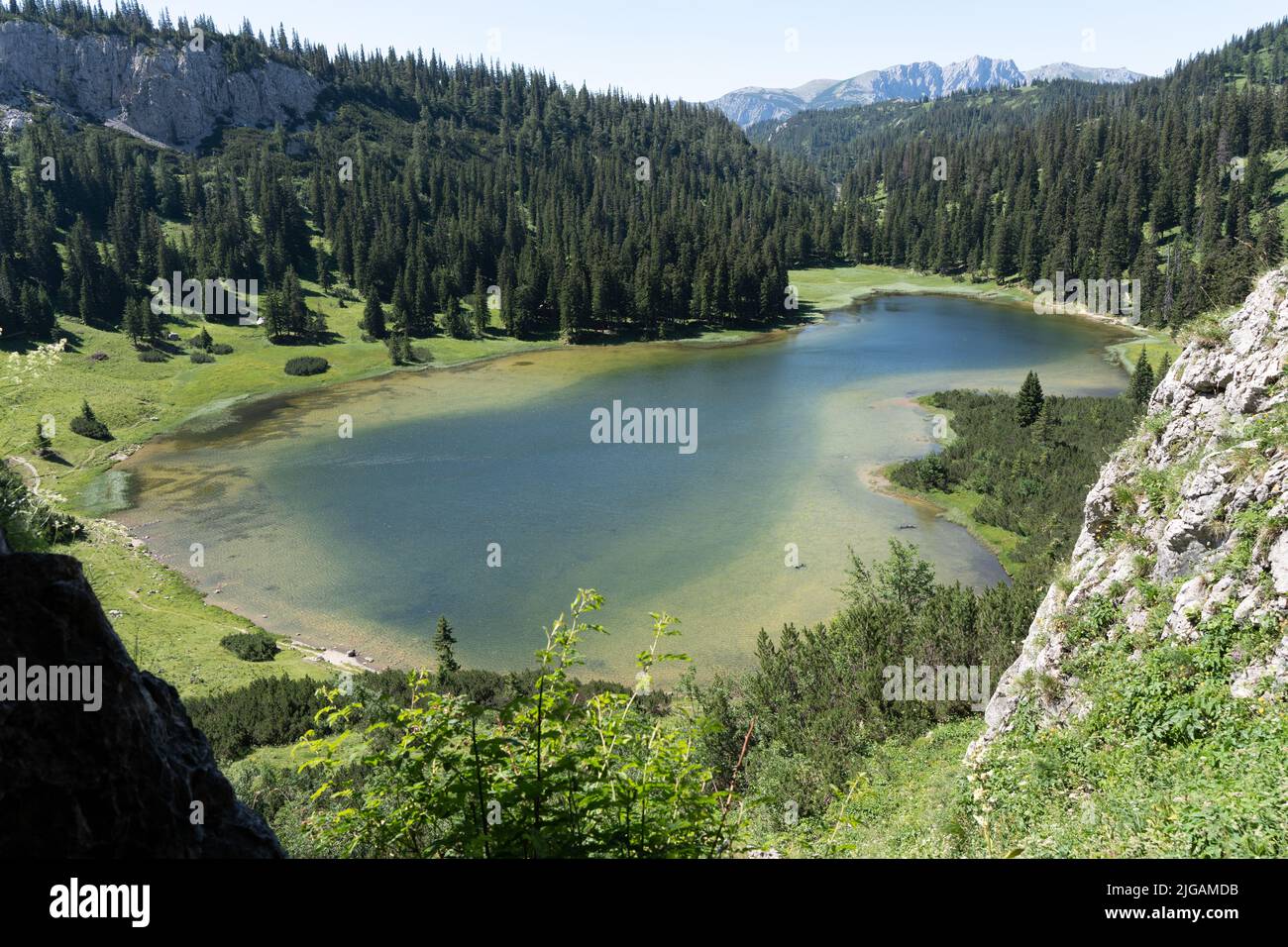 A scenic view of a lake surrounded by greenery and mountains on a sunny ...
