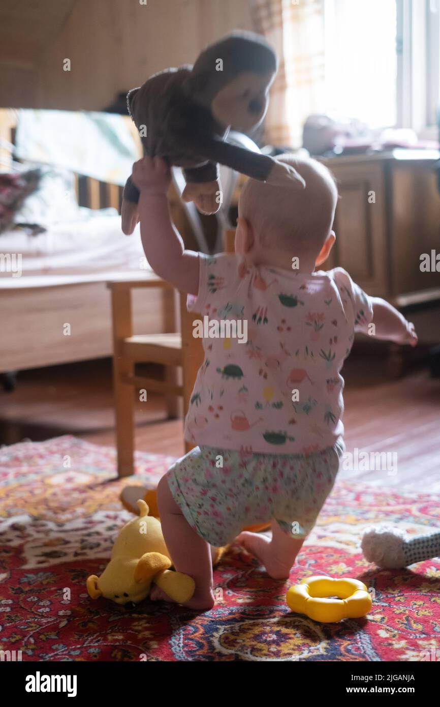 Little baby girl stands or climbs on the chair in the room. the baby is learning to walk Stock Photo