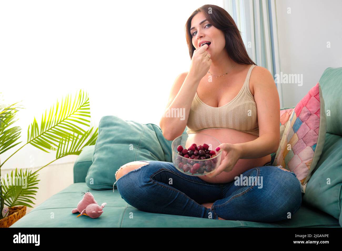 Pregnant young woman eating chips on the sofa at home. Food and cravings during pregnancy. Stock Photo