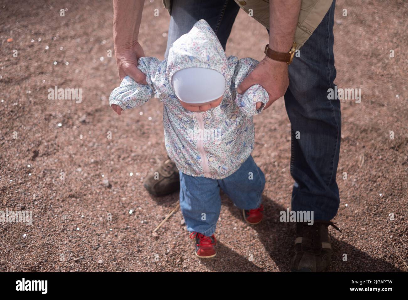 Little girl walking outdoors with man. Granfather helping his granddaughter to walk Stock Photo
