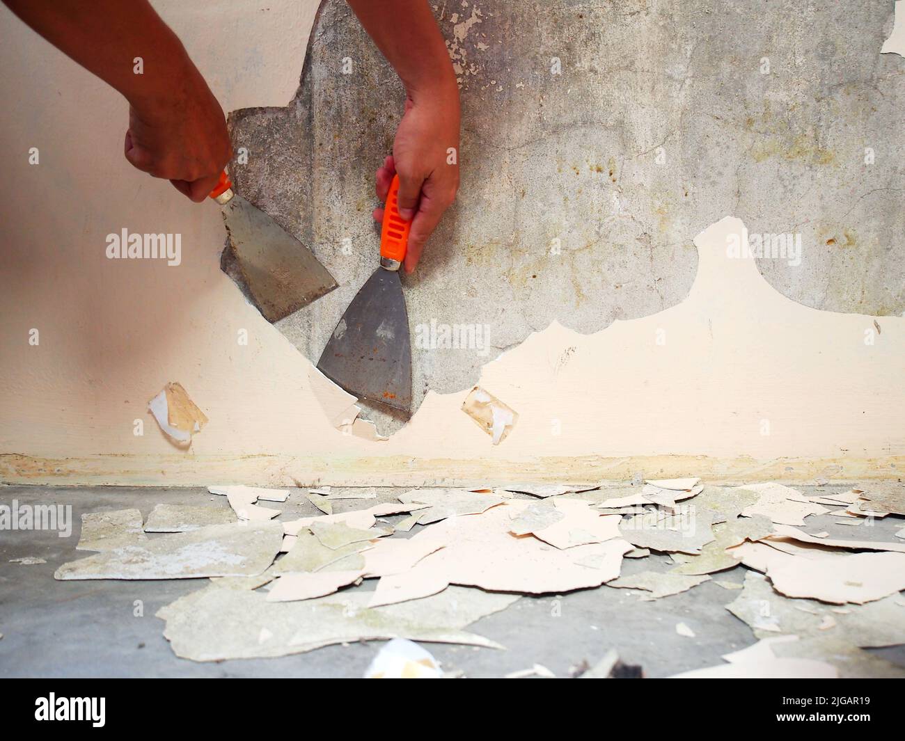 Removing old paint from the old wall by hand with a metal spatula
