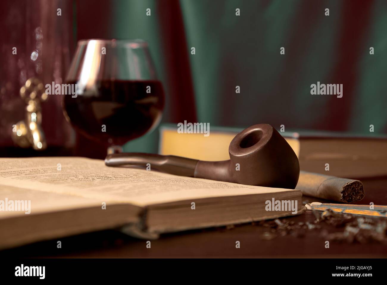 Dark toned image with smoking pipe, tobacco, book and brandy in the