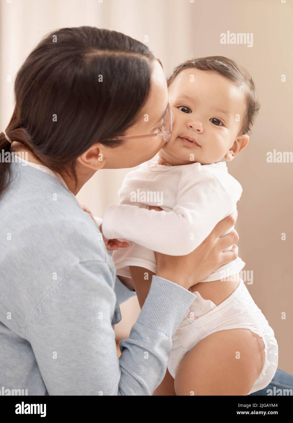 A whole lot of kisses make a happy baby. Portrait of an adorable baby girl being held and kissed by her mother at home. Stock Photo