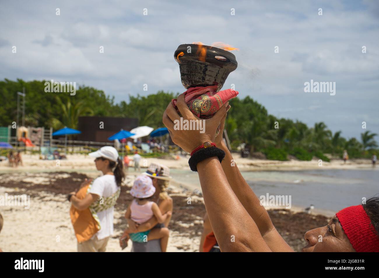 Latina woman with arms raised in a ceremony and a lit brazier in her hands at the beach in Mexico Stock Photo