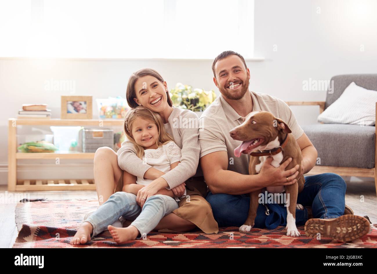 Our little family. Full length shot of a young family sitting with their dog on the living room floor at home. Stock Photo