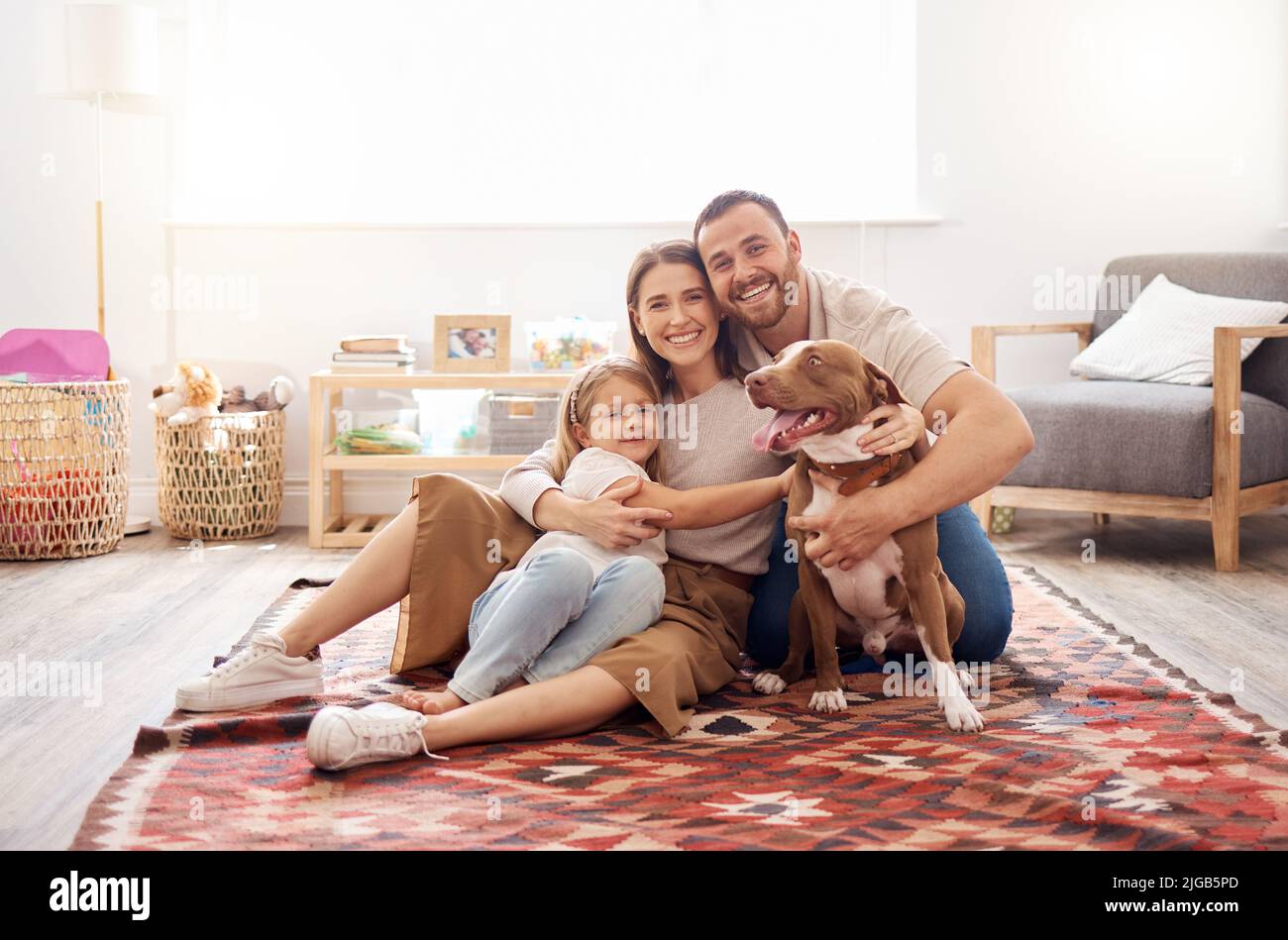 All we need is each other. Full length shot of a young family sitting with their dog on the living room floor at home. Stock Photo