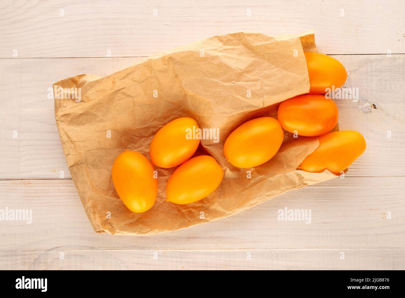 Several ripe yellow tomatoes with a paper bag on a wooden table, close-up, top view. Stock Photo