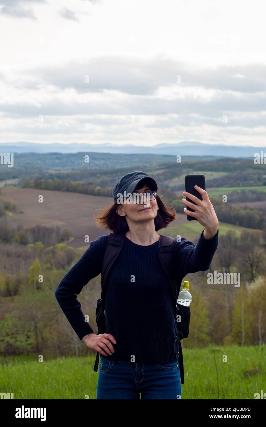Middle aged female model makes selfie on smartphone at mountain background Stock Photo