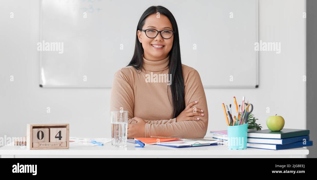 Asian female teacher sitting at table in classroom Stock Photo - Alamy