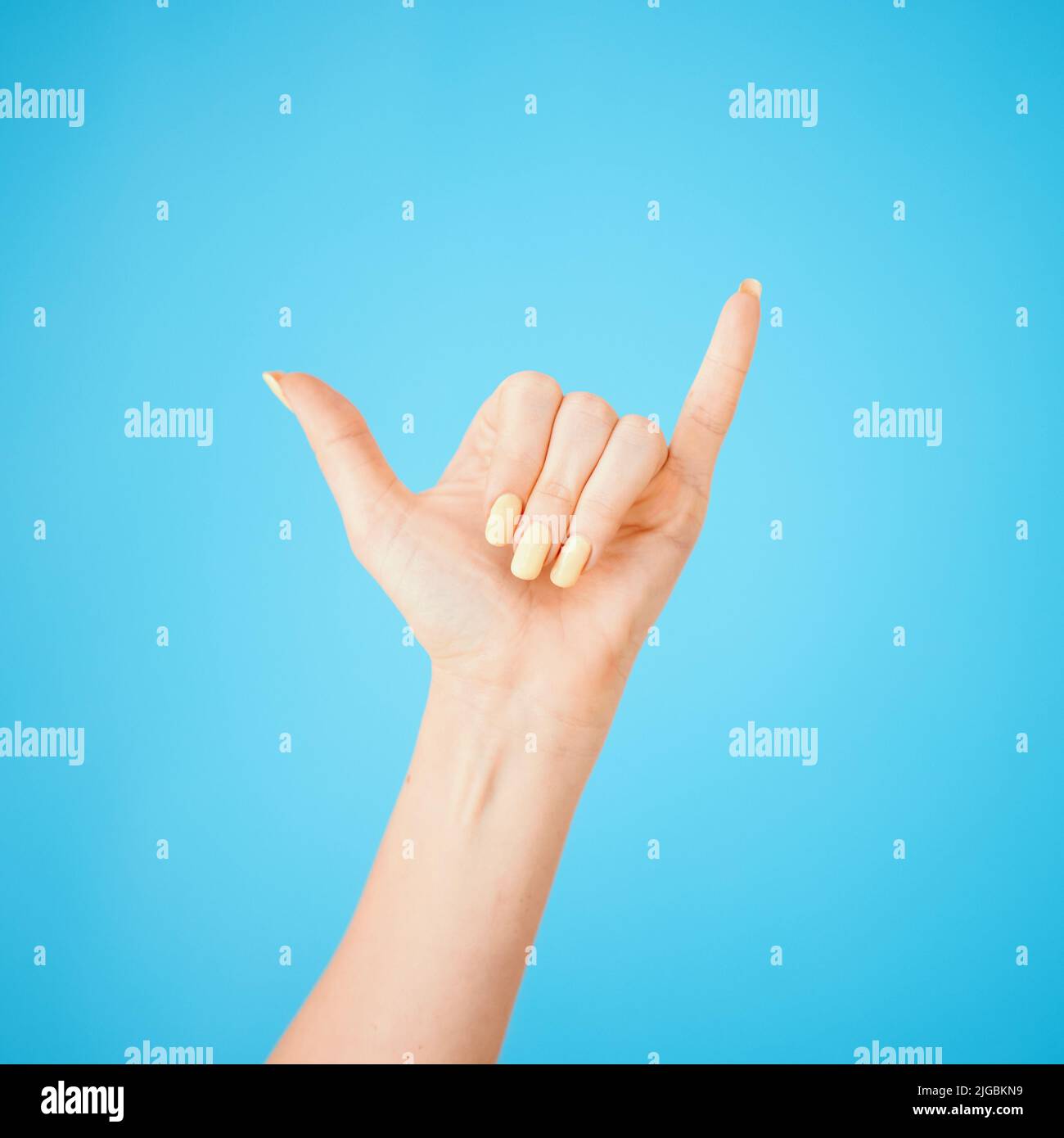 Hey, whats up. Studio shot of an unrecognisable woman showing a shaka hand sign against a blue background. Stock Photo