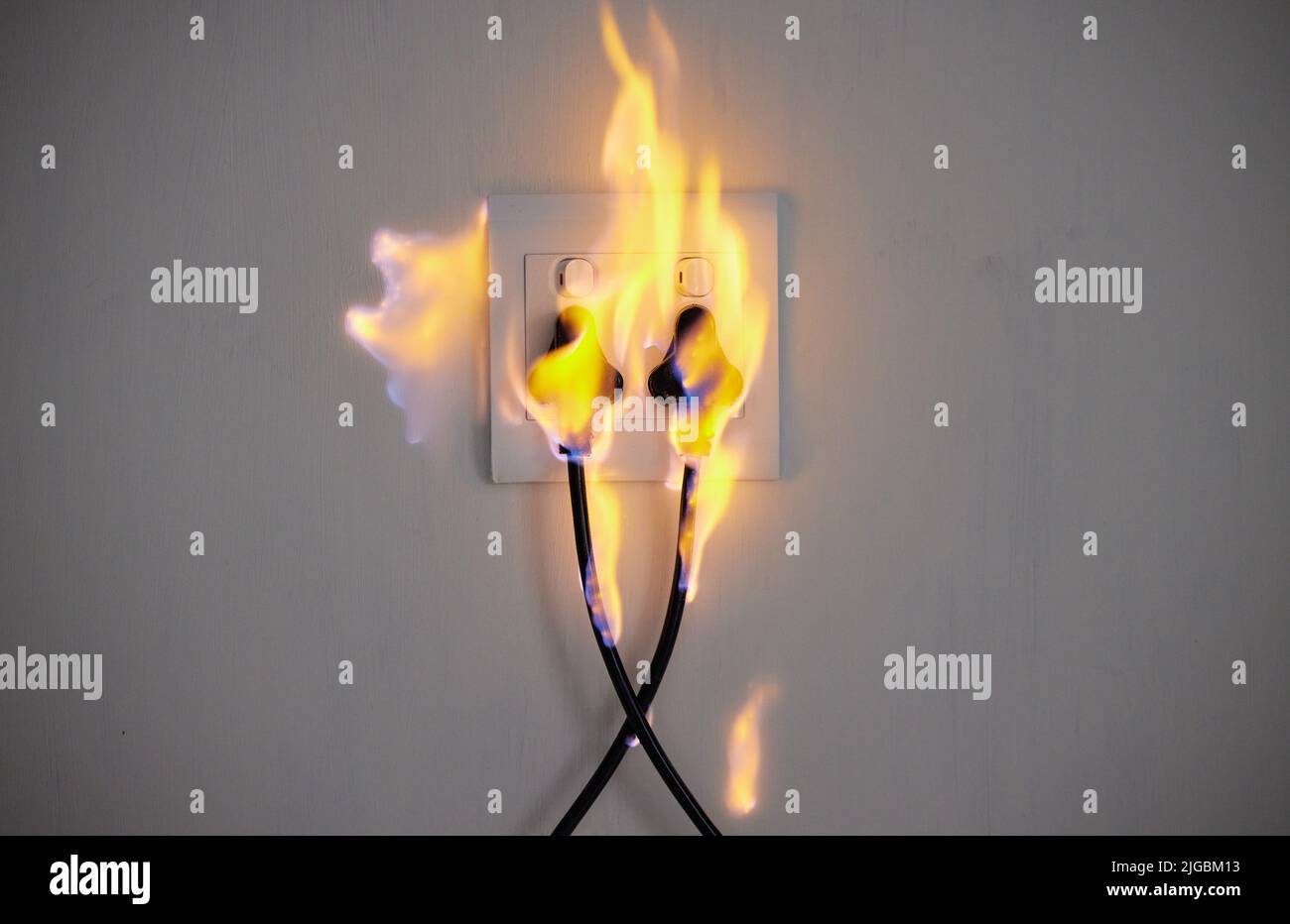 Electrical fire. two plugs in a wall socket catching fire Stock Photo