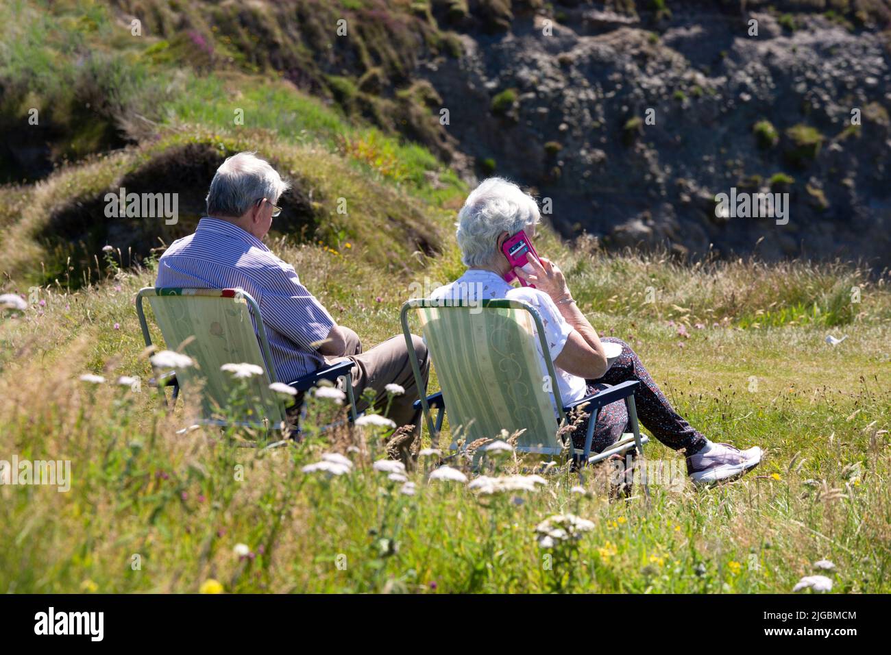 Senior couple sitting on garden chairs in long grass, Valentia Island, Kerry, Ireland Stock Photo