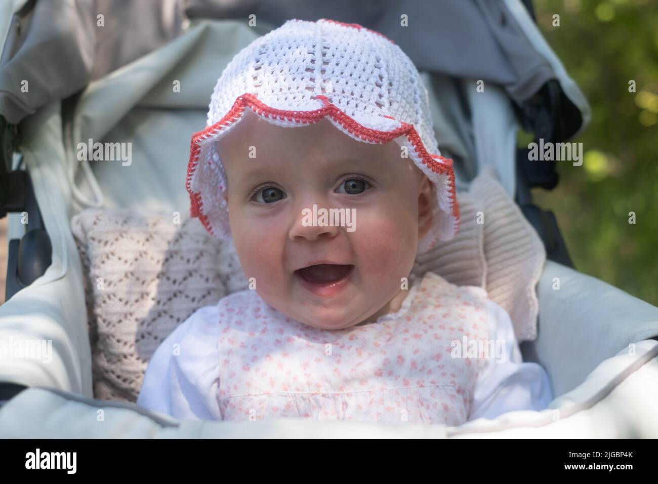 Seven month old baby child in white hat smiling looking at camera Stock Photo