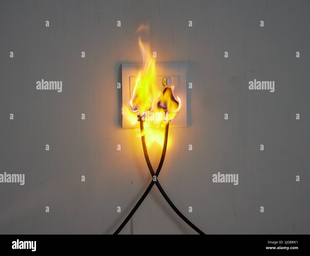 What a disaster. two plugs in a wall socket catching fire Stock Photo