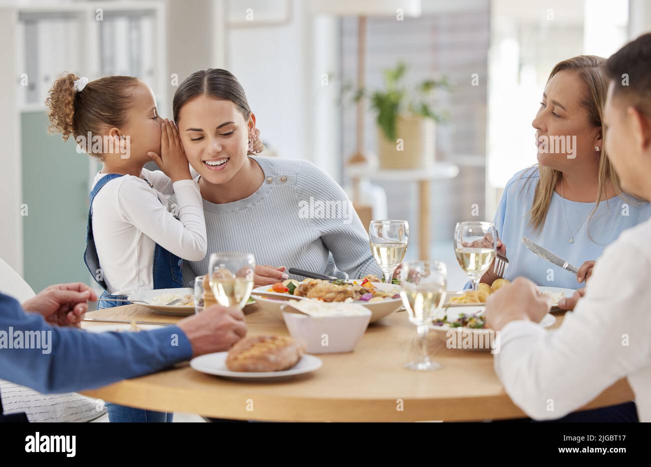 I need help in the potty. a little girl whispering a secret in her mothers ear while having lunch with her family at home. Stock Photo