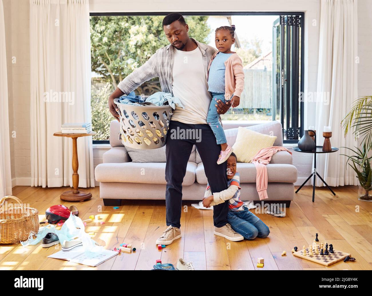This day has been too long. a little boy throwing a tantrum while holding his parents leg at home. Stock Photo
