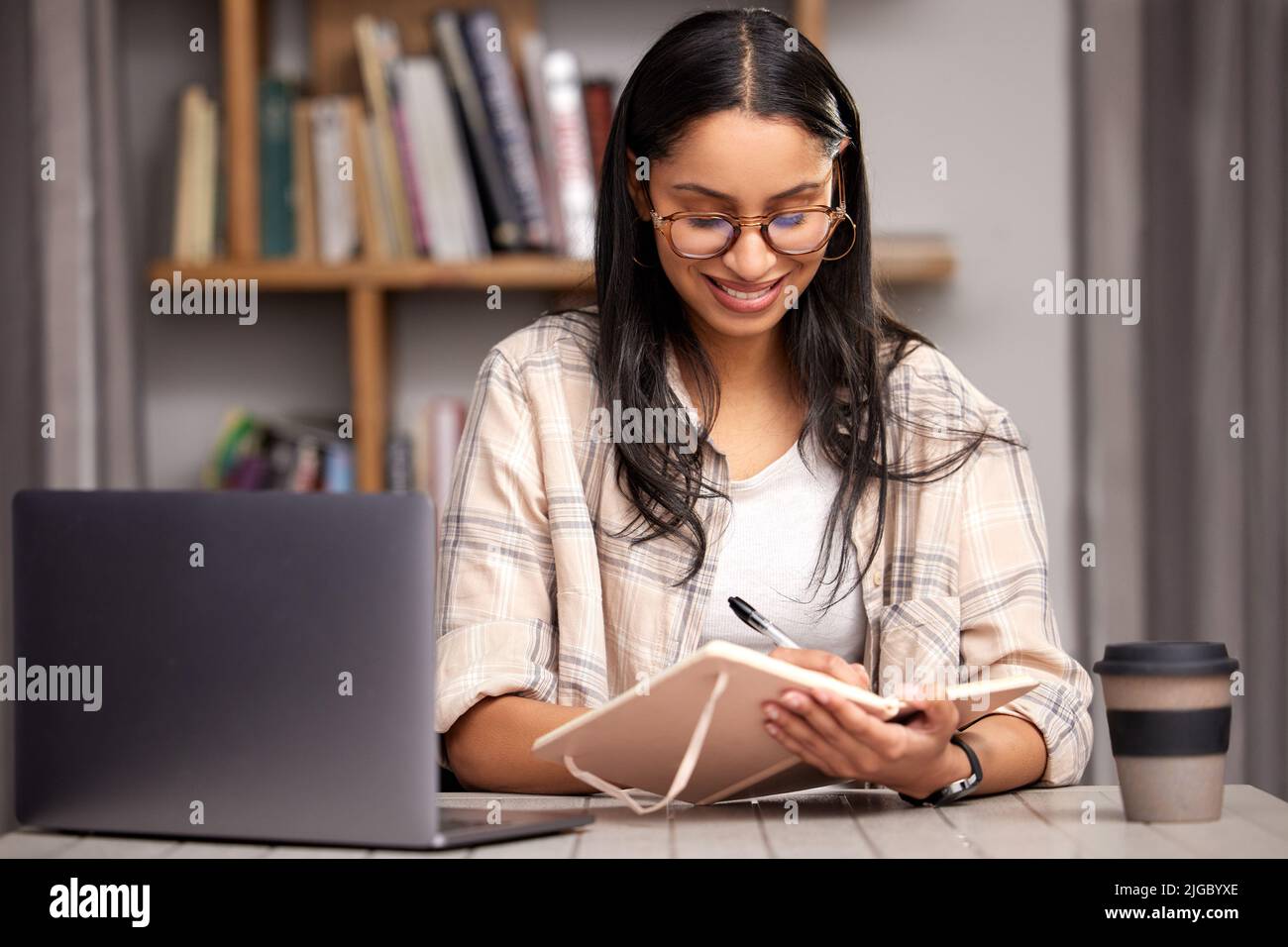 Shes fully prepped for finals. an attractive young female student taking notes while studying in the library using her laptop. Stock Photo