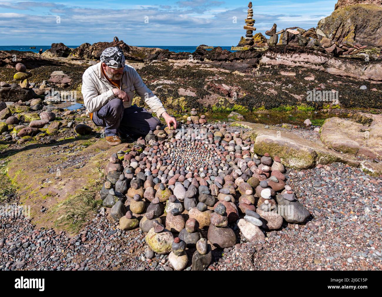 Dunbar, East Lothian, Scotland, UK, 9th July 2022. European Stone Stacking Championship: participants have 3.5 hours to create an artistic artwork from the rocks on Eye Cave Beach. Pictured: James Brunt, land artist Stock Photo