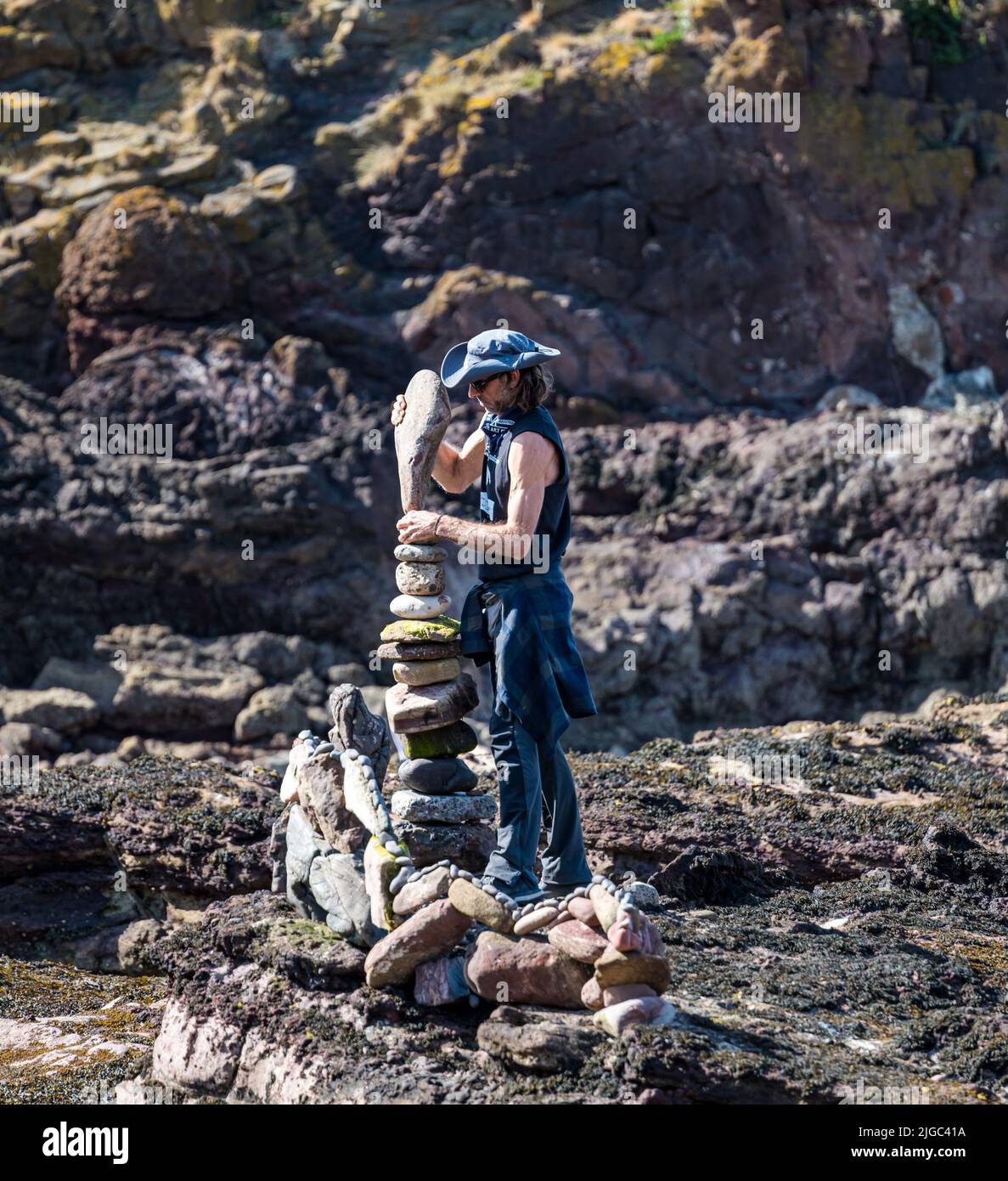 Dunbar, East Lothian, Scotland, UK, 9th July 2022. European Stone Stacking Championship: participants have 3.5 hours to create an artistic artwork from the rocks on Eye Cave Beach. Pictured: Pedro Duran, stone stacker Stock Photo