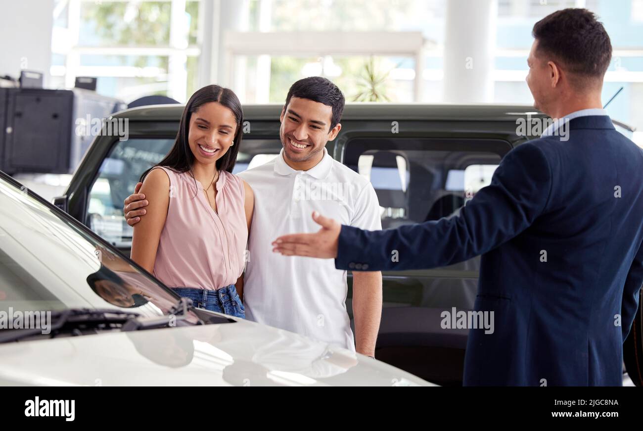 This beauty just came in. a car salesman assisting a young couple on the showroom floor. Stock Photo