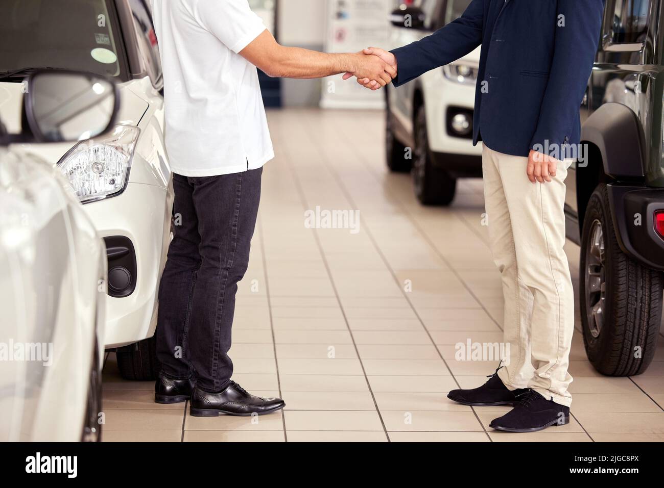 Well make your car dreams come true. a car salesman shaking hands with a client on the showroom floor. Stock Photo