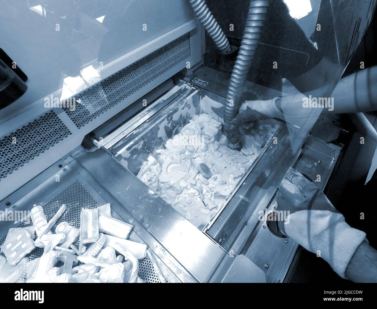 A man working with a working vacuum cleaner to clean the white powder of polyamide from a model printed on a 3D printer inside a 3D printer. Cleaning objects printed on an industrial powder 3D printer Stock Photo