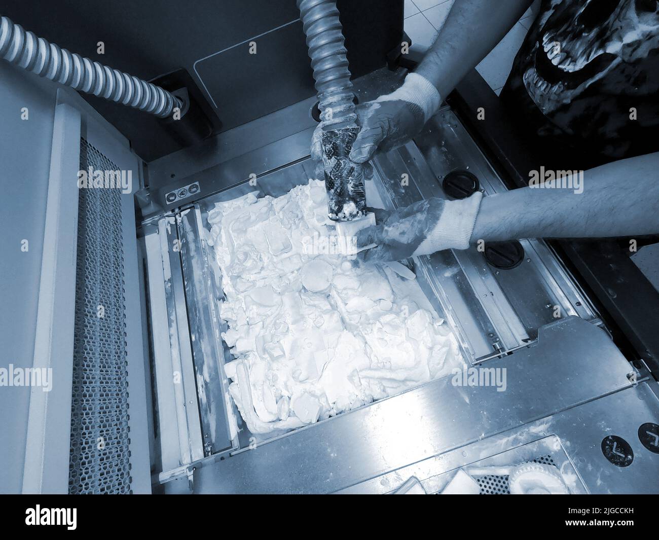 A man working with a working vacuum cleaner to clean the white powder of polyamide from a model printed on a 3D printer inside a 3D printer. Cleaning objects printed on an industrial powder 3D printer Stock Photo