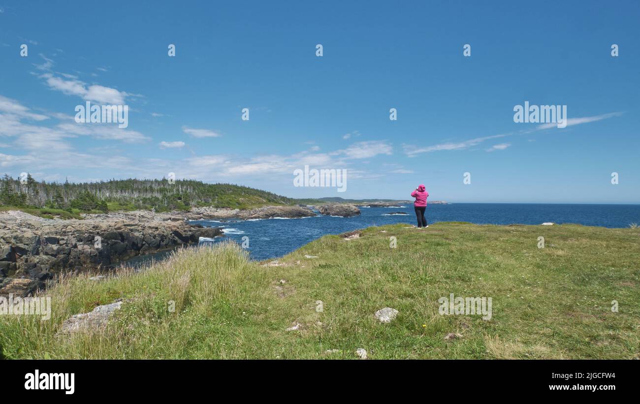 Woman is dwarfed by the beautiful rugged coast of Cape Breton while taking photographs. Stock Photo