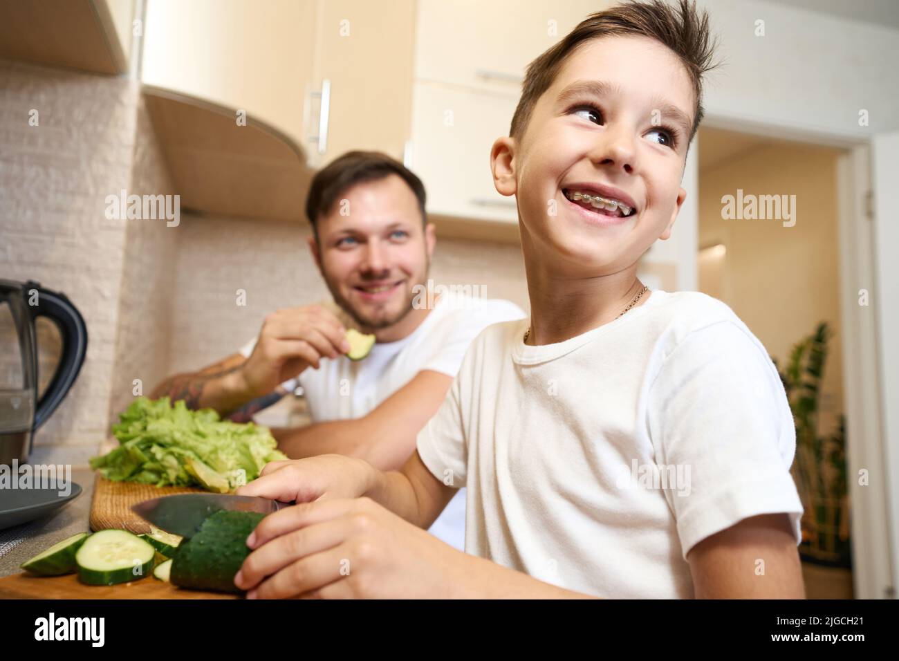 Boy with teeth braces smiling while cutting cucumber Stock Photo - Alamy
