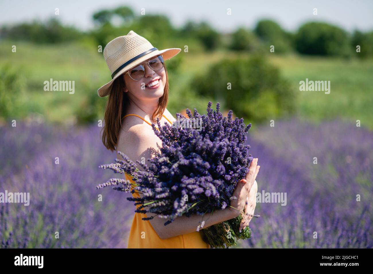 A woman in a yellow dress and a straw hat with a huge bouquet of ...