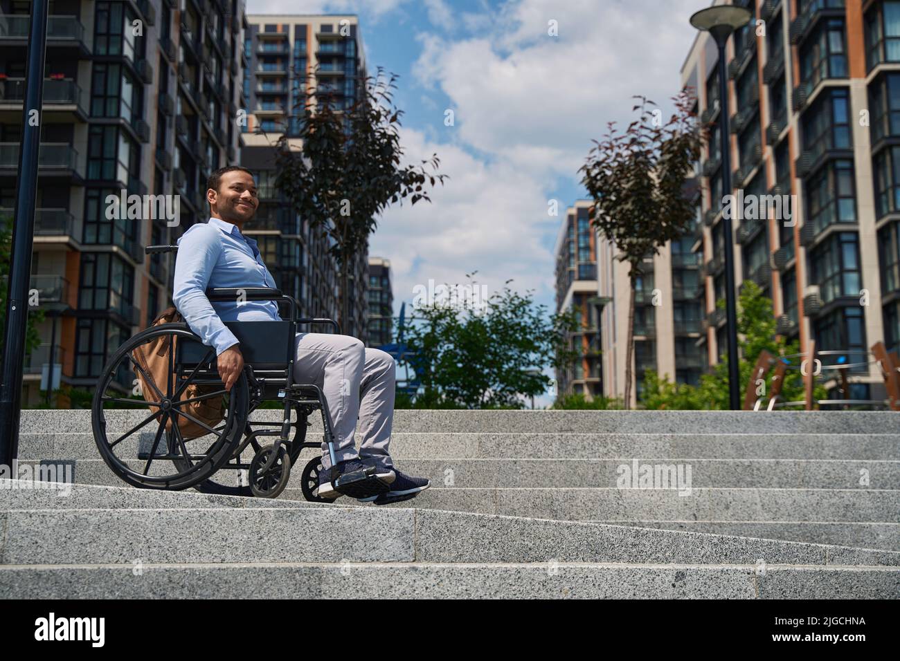 Joyous wheelchair-bound male person descending stairs outdoors Stock Photo