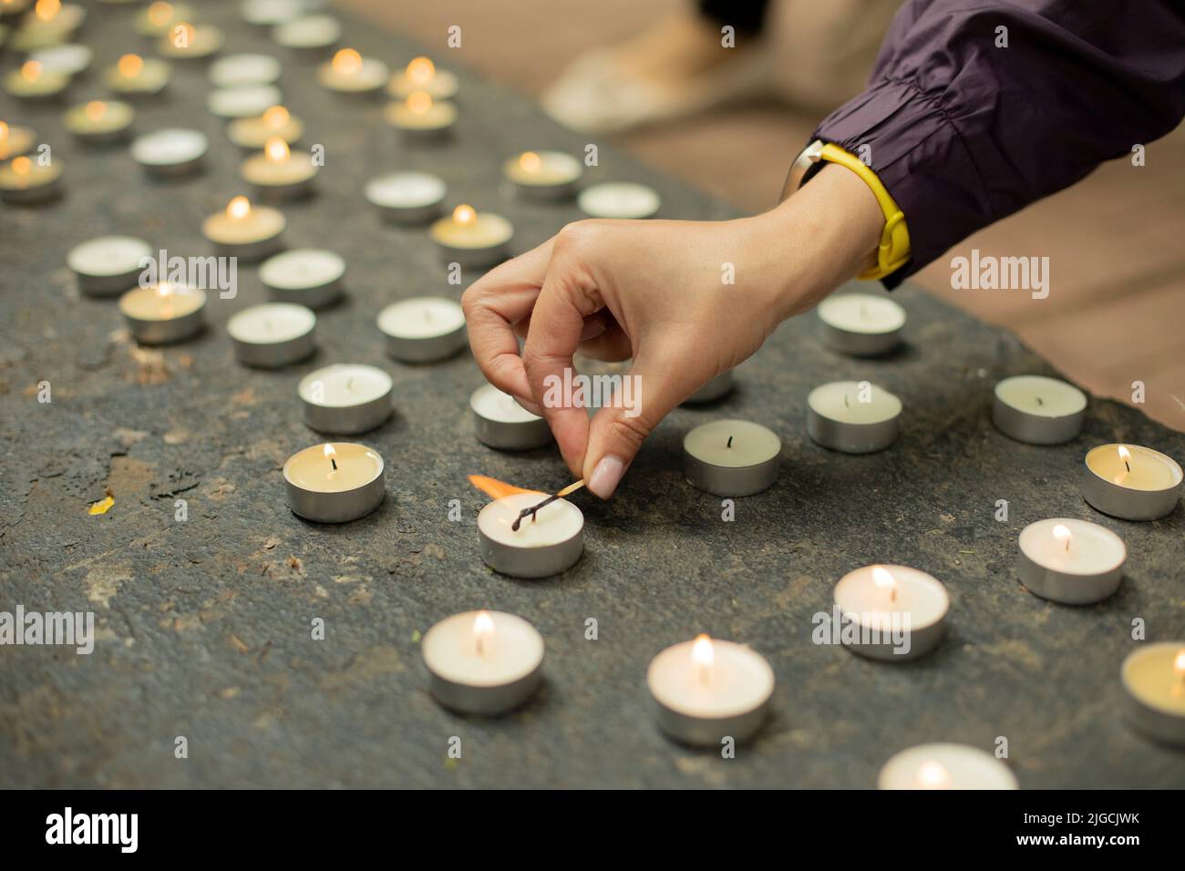 Lighting candle on grave. Lots of candles. Match burns in hand. Details