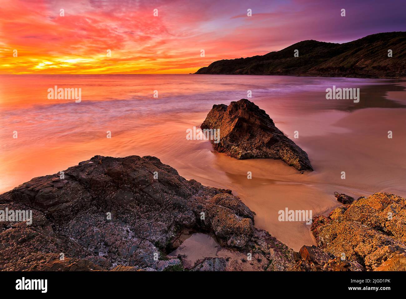 Bright hot red sunrise over Pacific ocean at Forster town Burgess beach with scenic rock cliffs and smooth sand. Stock Photo