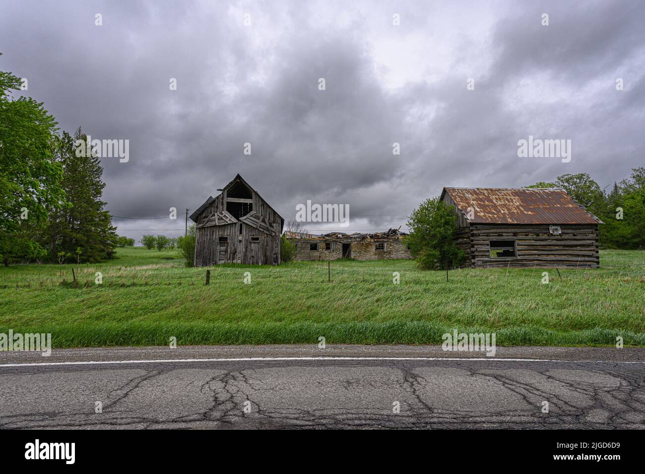 Collapsed farm house sits between two farm buildings Stock Photo