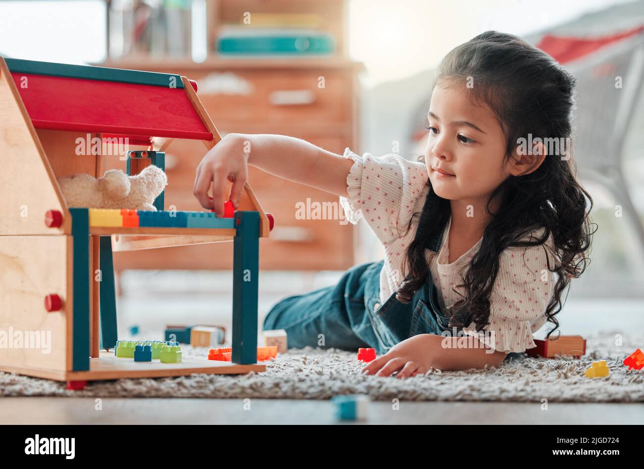 Ill make it more cozy for you Teddy. an adorable little girl playing a dollhouse. Stock Photo