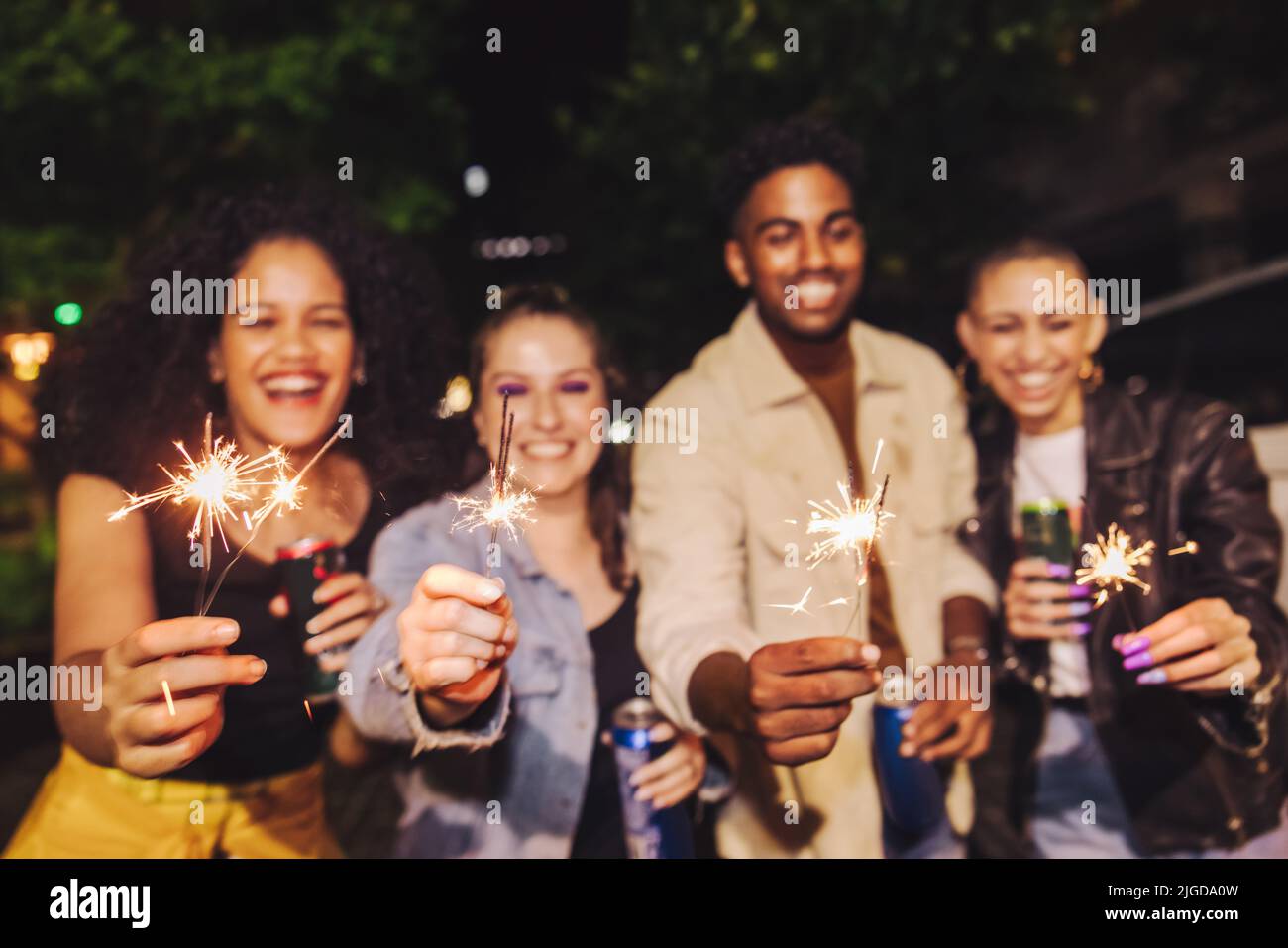 Bengal lights for the holiday season. Four happy young people holding up their sparklers at night. Group of cheerful friends having a good time while Stock Photo