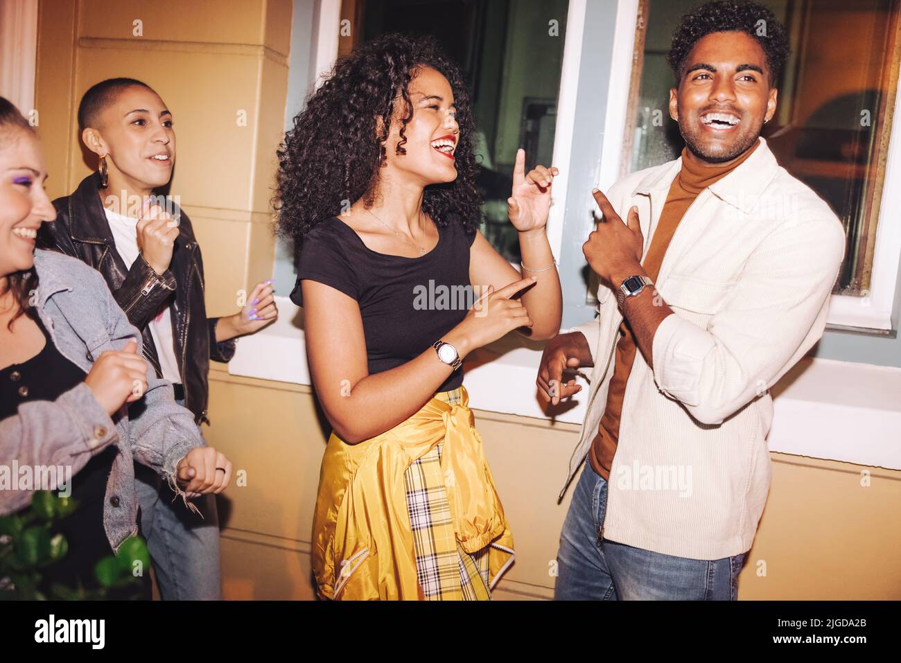 Group of happy young friends singing and dancing to their favourite song outdoors. Multicultural young people having a good time while hanging out tog Stock Photo