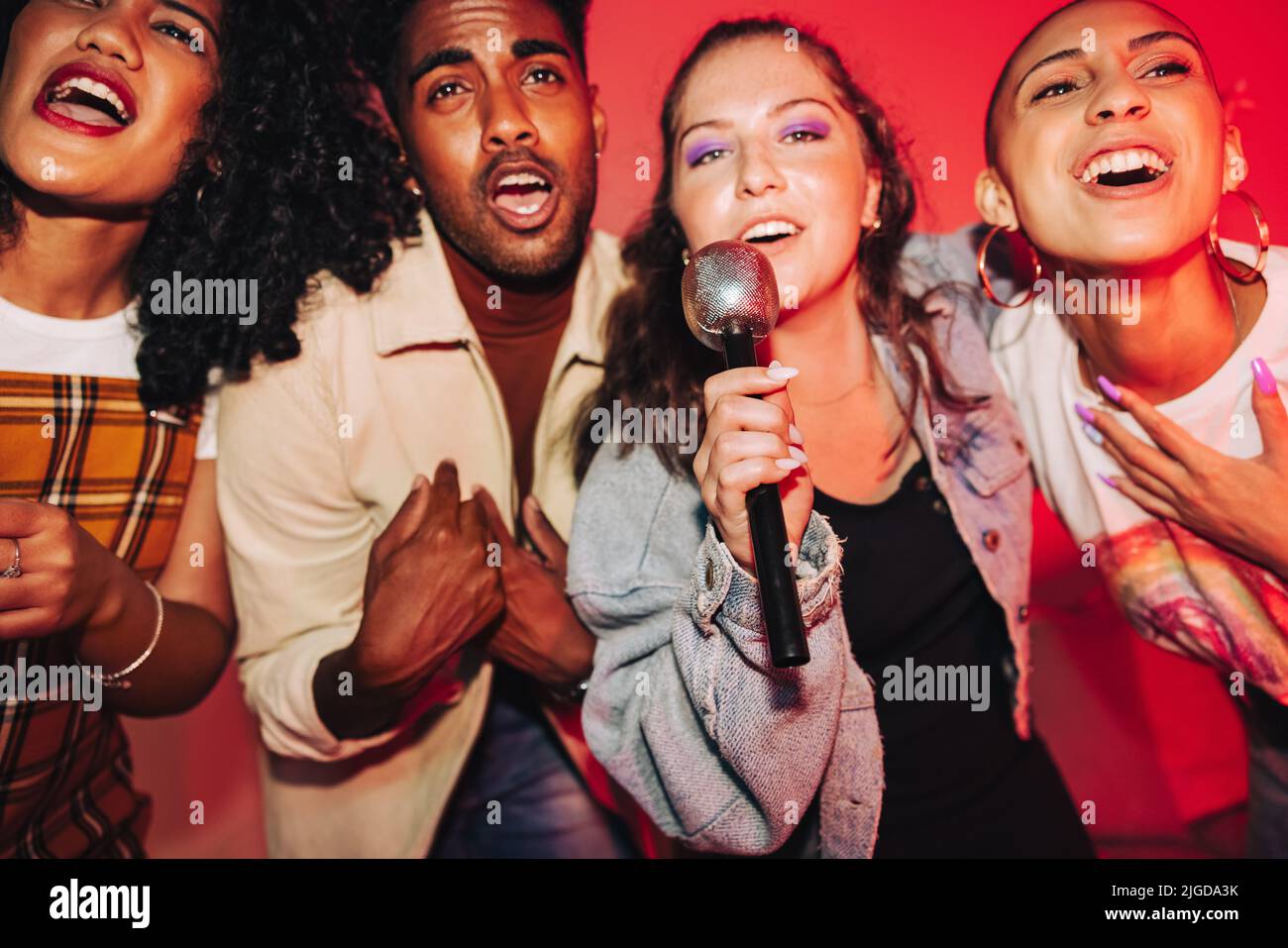 Vibrant friends singing together on karaoke night. Group of cheerful friends singing their favourite song at a house party. Multicultural friends havi Stock Photo