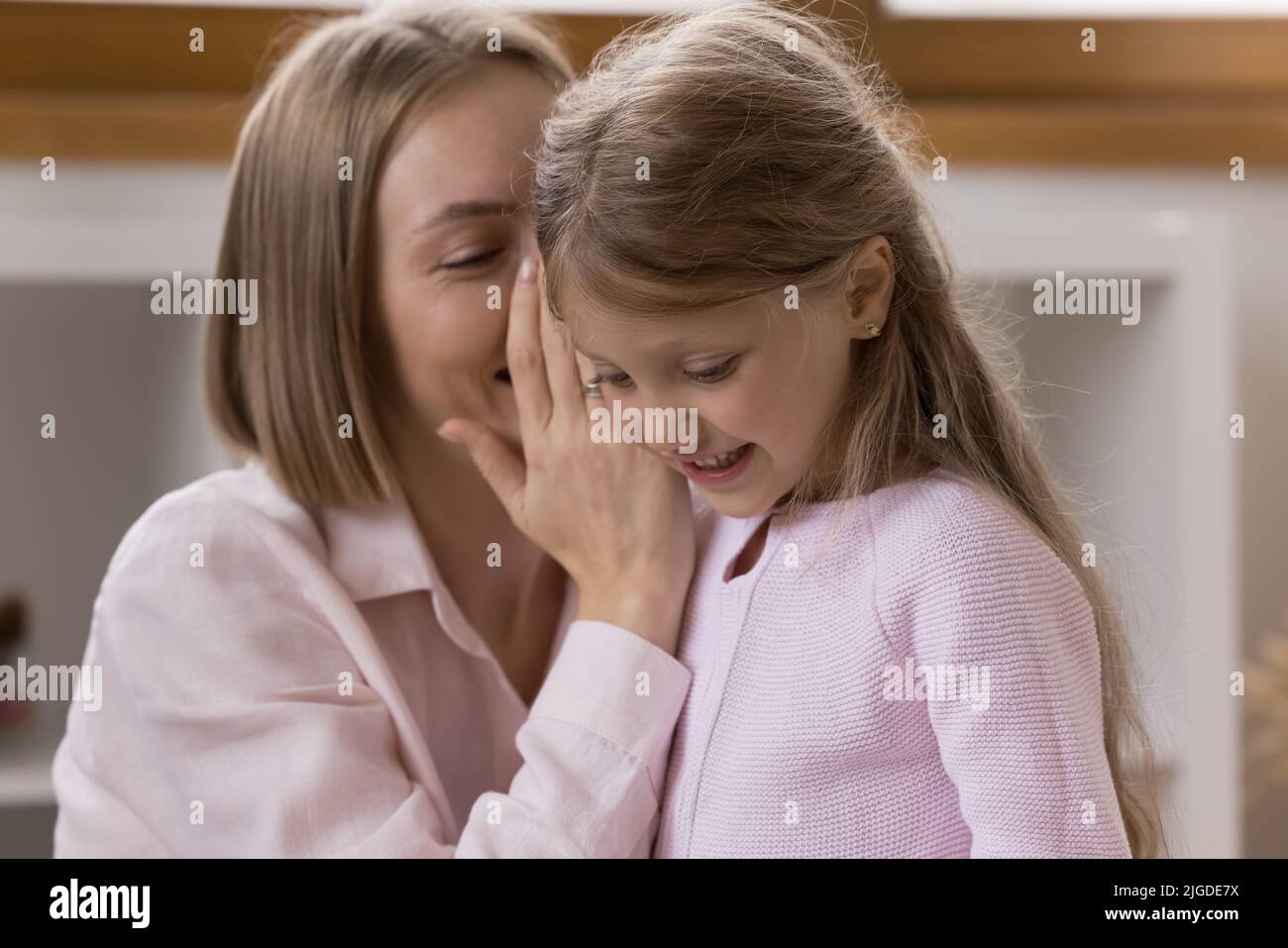 Happy mother telling secret to daughter, whispering in kids ear Stock Photo