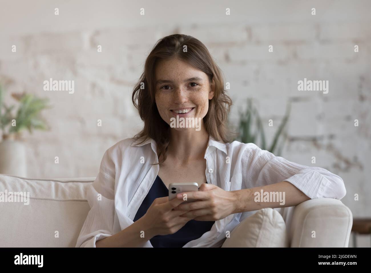 Attractive woman sit on sofa with modern smartphone Stock Photo