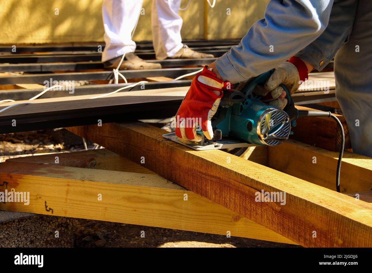 Carpenter uses an electric circular saw to cut a beam. Stock Photo